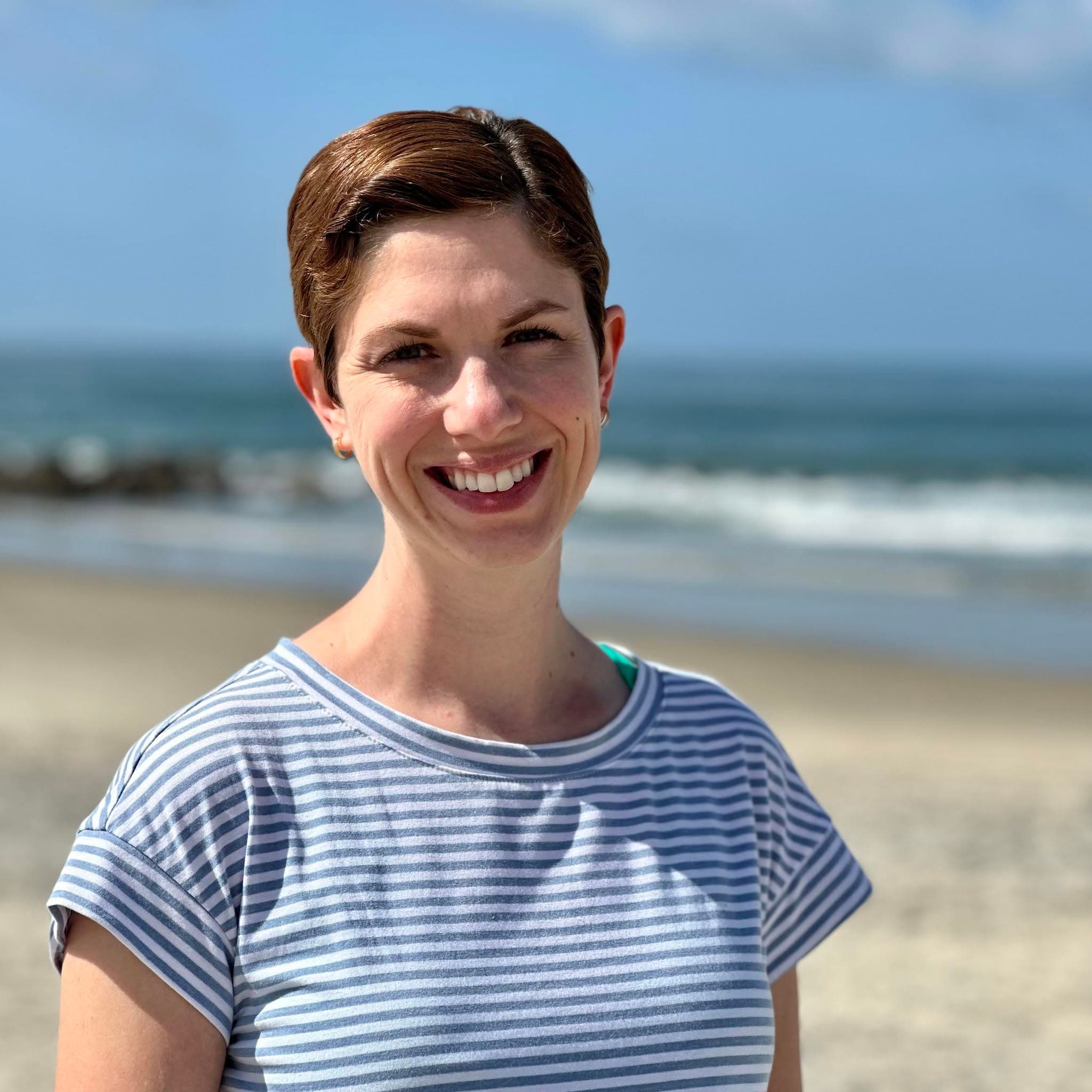 Brooke Millward, founder of Citravia Travel, smiling on a beach with the ocean behind her